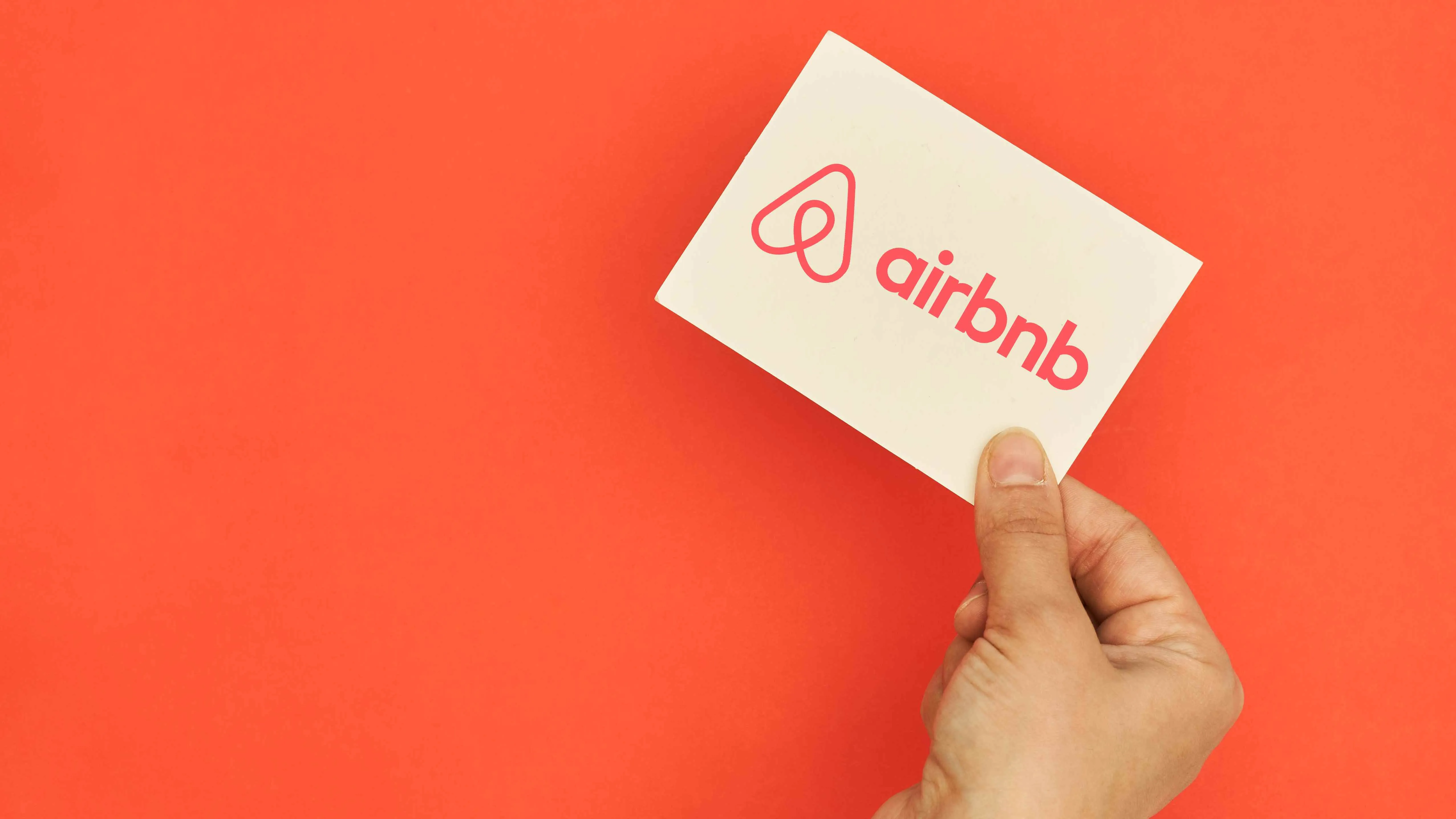 Hand holds Airbnb logo card over red background
